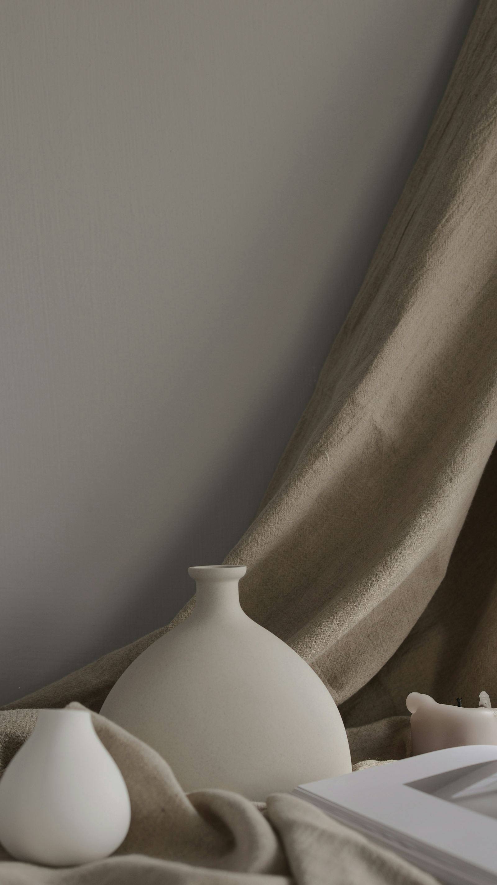Vase en céramique blanche et rideau en lin drapé, détail de décoration d'un appartement près de Saint-Malo