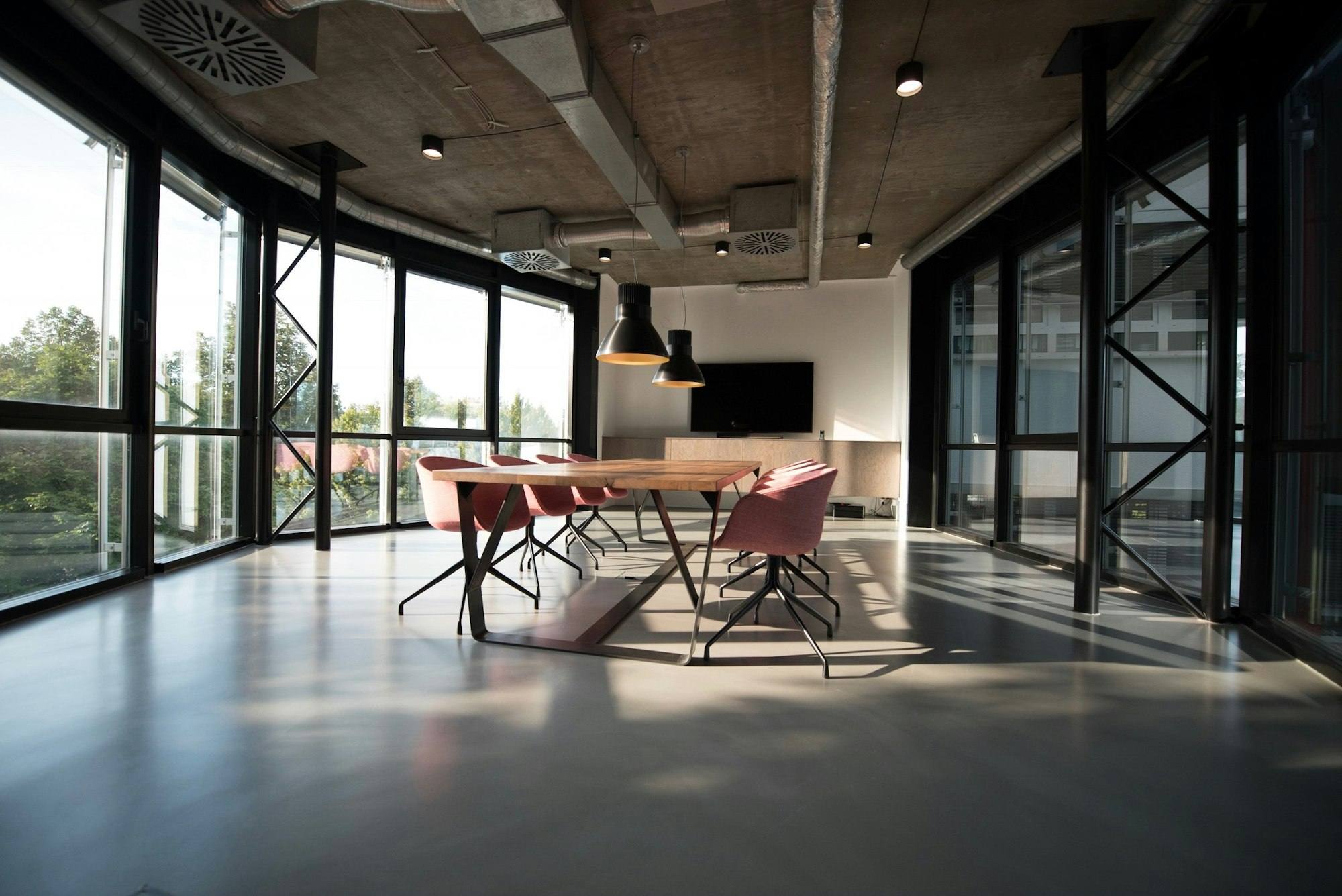 Salle de réunion vitrée avec grande table en bois et chaises roses, bureaux de Saint-Brieuc