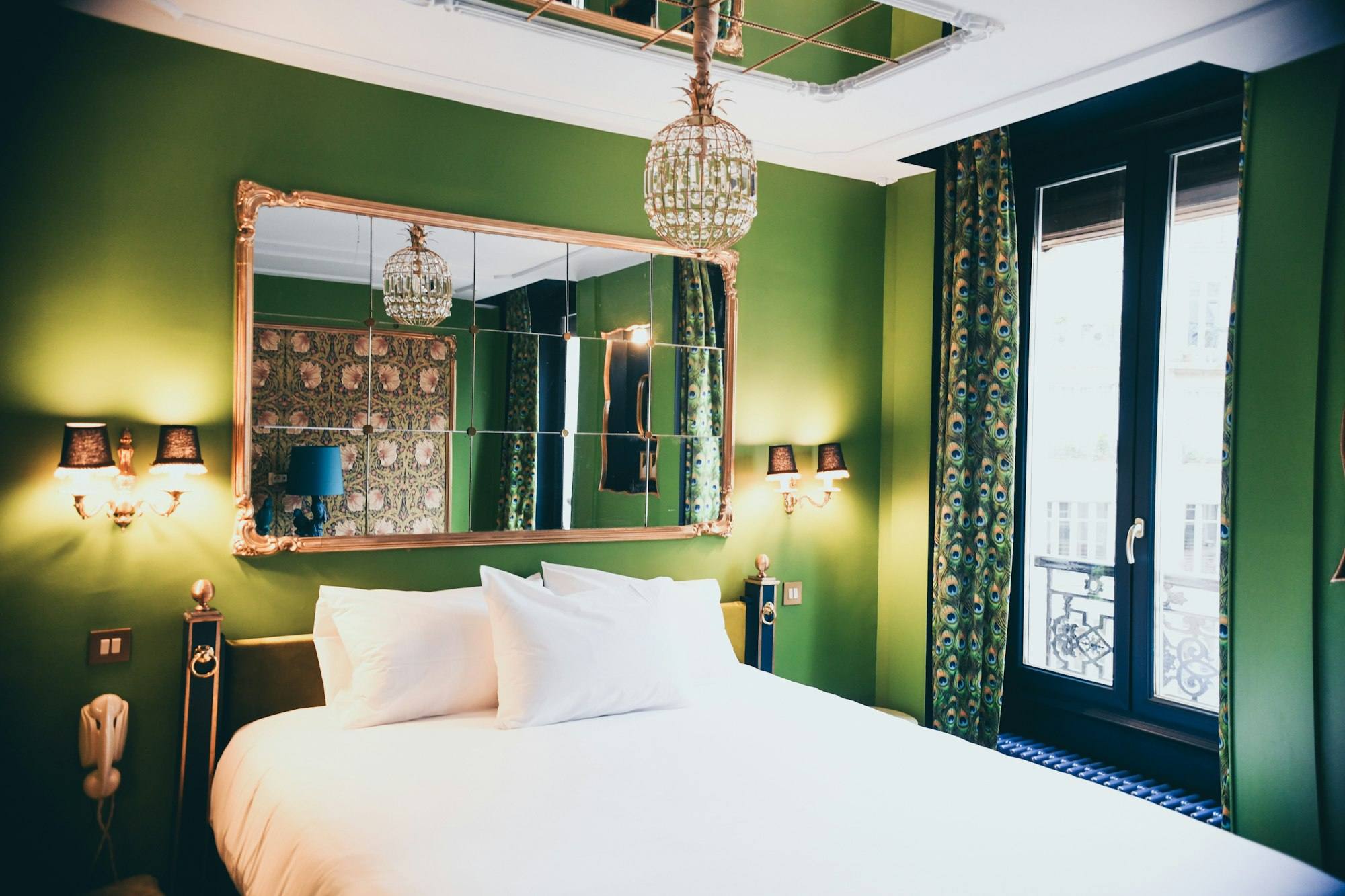 Chambre vert profond avec miroir doré, lit blanc et rideaux à motif paon, hôtel de Saint-Malo