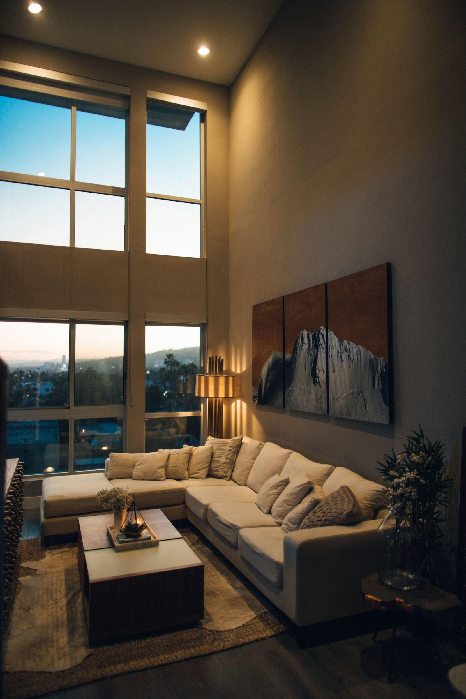 Séjour aux baies vitrées toute hauteur avec canapé beige et tableau mural, loft rennais en soirée