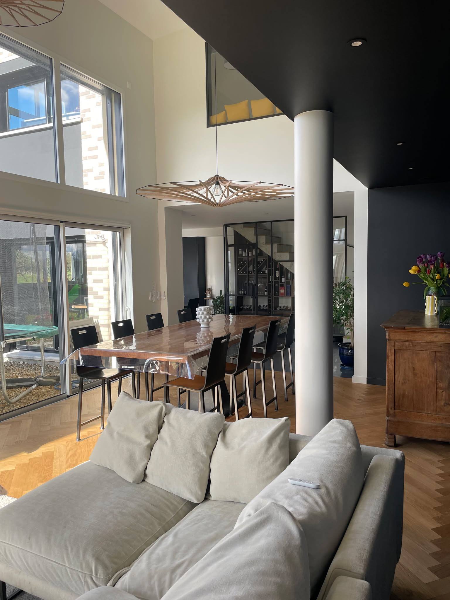 Séjour vu depuis la mezzanine, canapé blanc et baies vitrées ouvertes sur le jardin, poteau blanc et mur bleu nuit