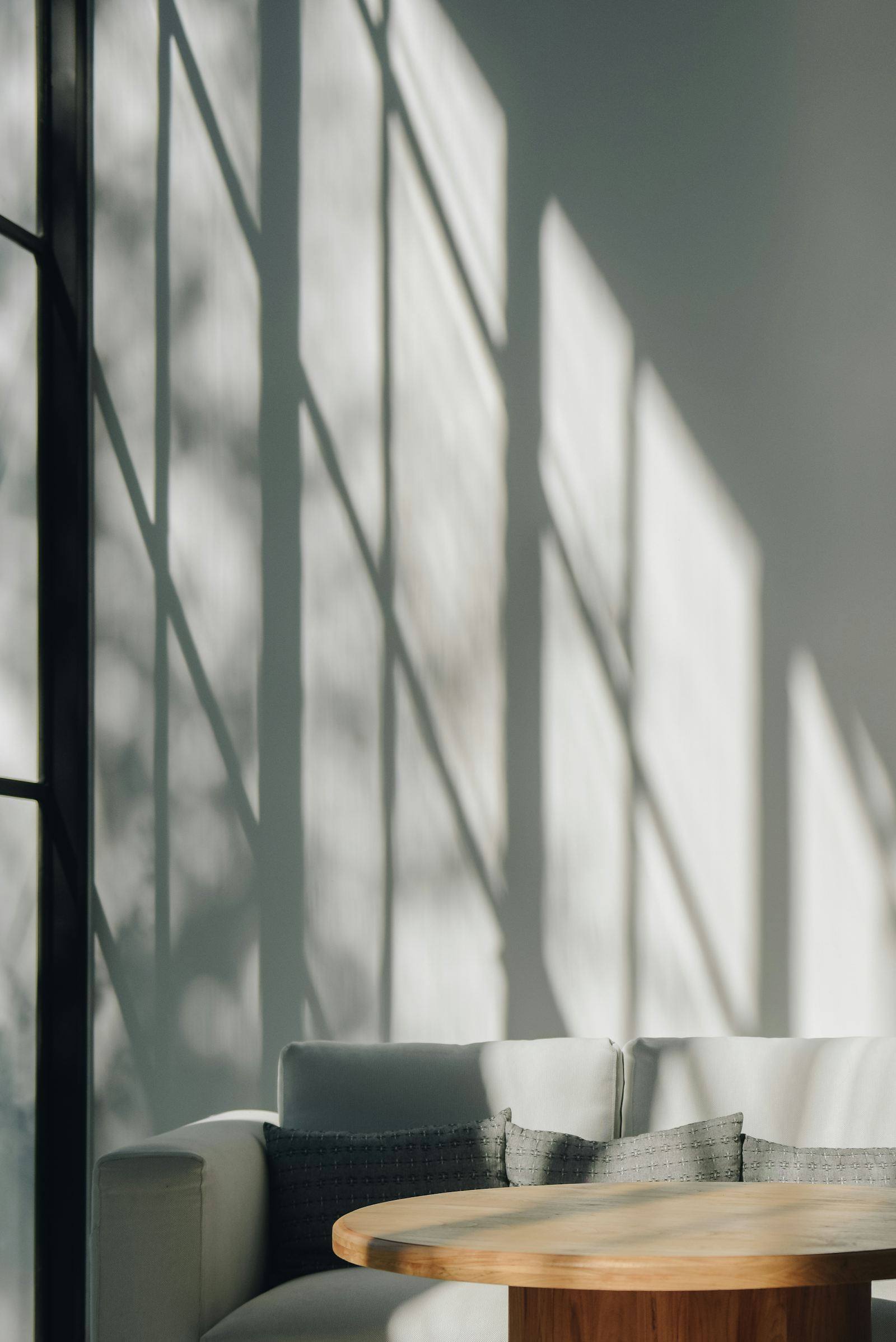 Jeu de lumière traversant des stores sur un canapé gris et une table basse en bois, maison à Laval