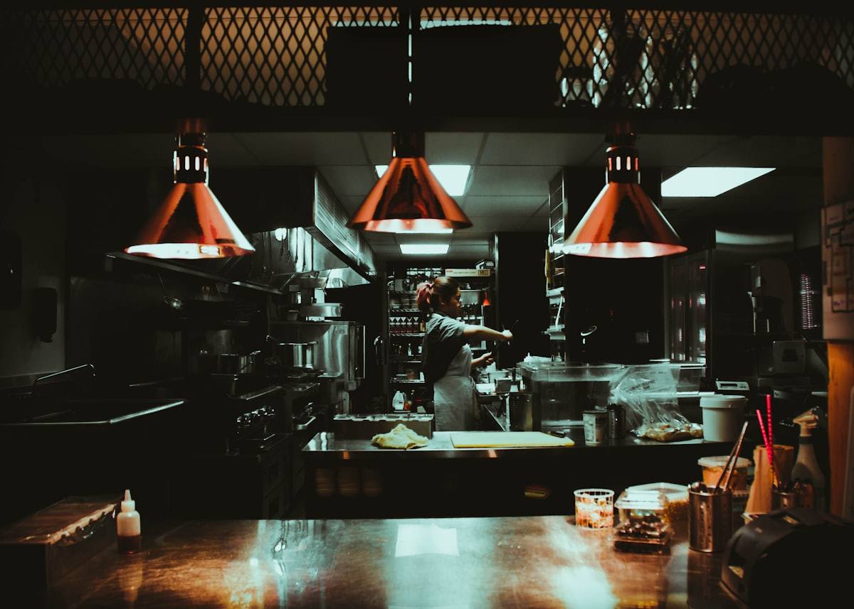 Cuisine ouverte de nuit avec suspensions orange et cuisinier en plein service, restaurant à Dinan