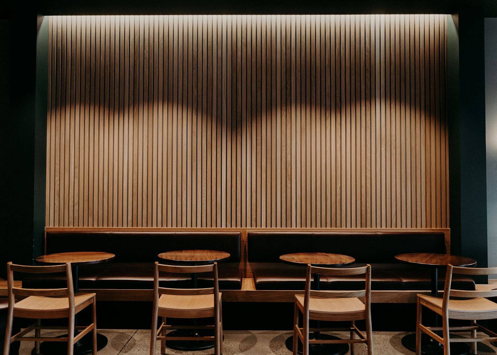 Banquette contre un mur cannelé en bois clair avec petites tables rondes, restaurant à Dinan