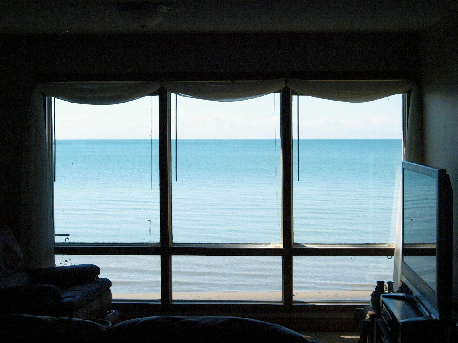Séjour sombre avec grande baie vitrée ouverte sur une mer calme, villa rénovée face à la baie de Dinard