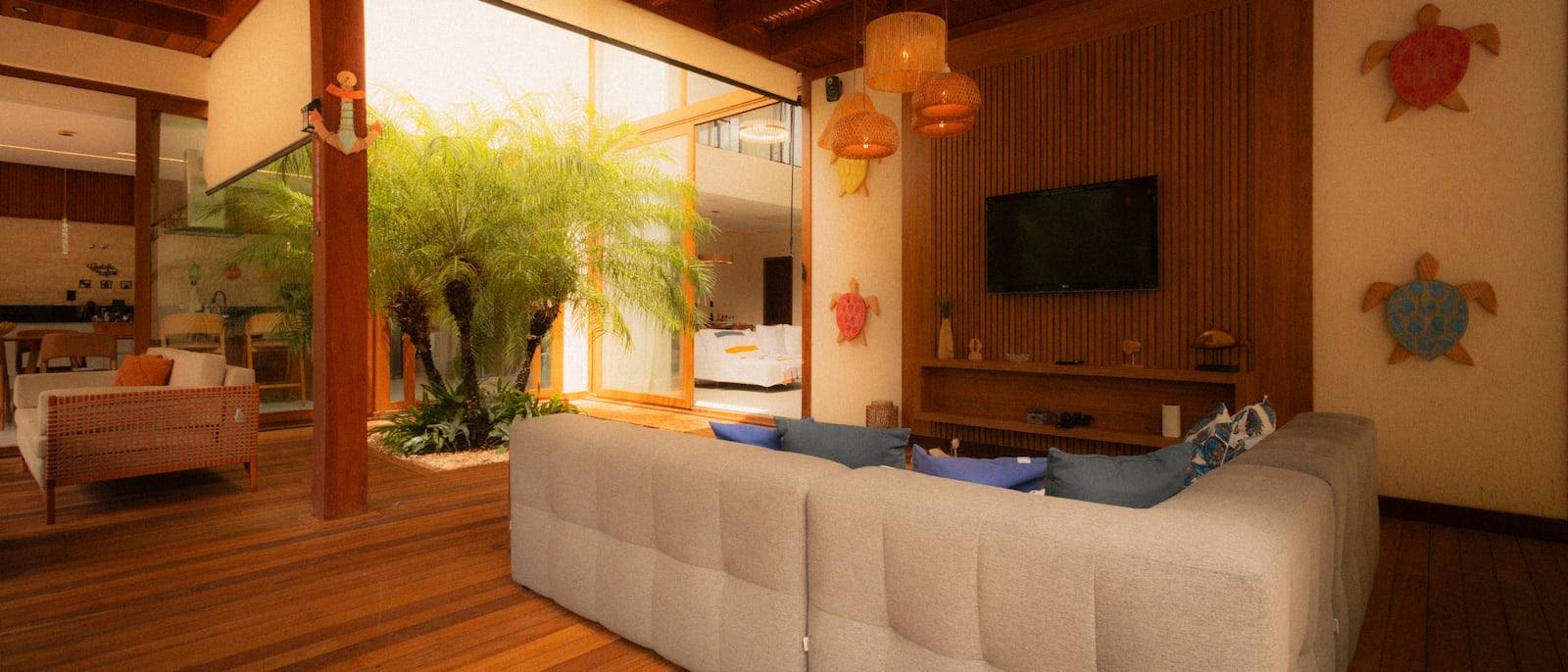 Salon avec canapé en lin clair, colonnes en bois et palmier en pot, villa rénovée près de Dinard